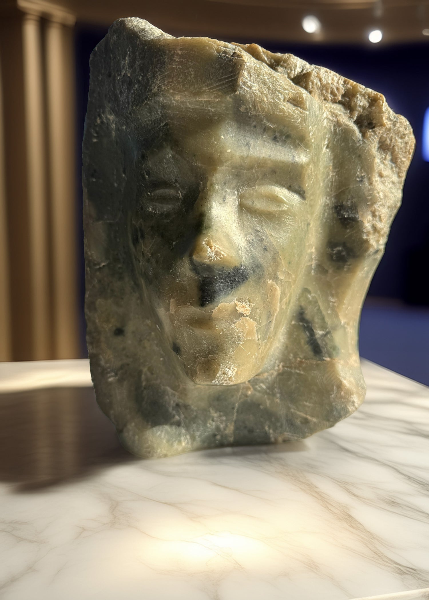 Serpentine carving by Chaim Gross titled ‘Head of a Woman,’ featuring a stylized female face emerging from a roughly hewn block of green and amber-toned serpentine stone